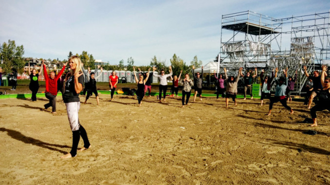 A woman standing in a sandpit leading a group of people in yoga poses