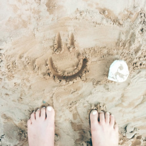 Toes in sand with a happy face drawn in it. 