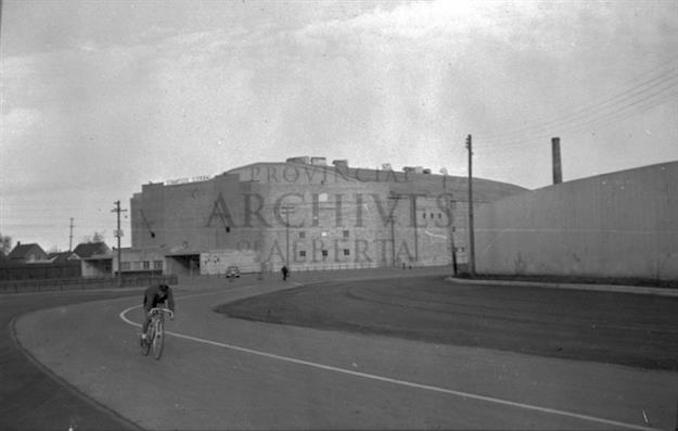 1952-Tom Smith riding bicycle outside of Stampede Corral, Calgary